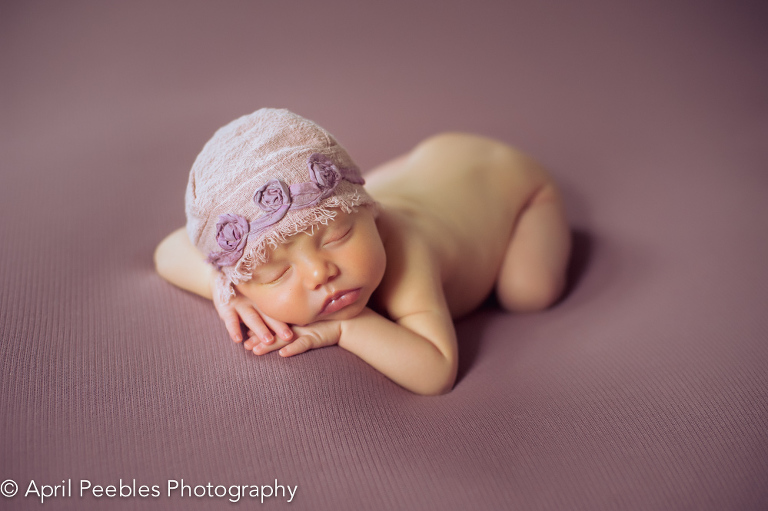 Newborn image wearing purple flower hat